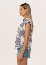 [Color: White/Navy] A side facing image of a blonde model wearing a summer top in a blue and white vintage floral print. With short cap sleeves, a split v neckline with tassel ties, and a contrast crochet edge stitch trim.