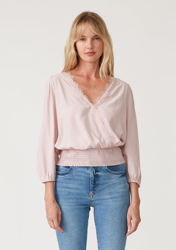 [Color: Dusty Pink] A front facing image of a blonde model wearing a dusty pink bohemian resort top with three quarter length sleeves, a surplice v neckline with lace trim, and a smocked elastic waist. 