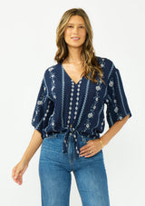 [Color: Navy/Blue] A front facing image of a brunette model wearing a blue embroidered tie front top with half length sleeves and a v neckline. 