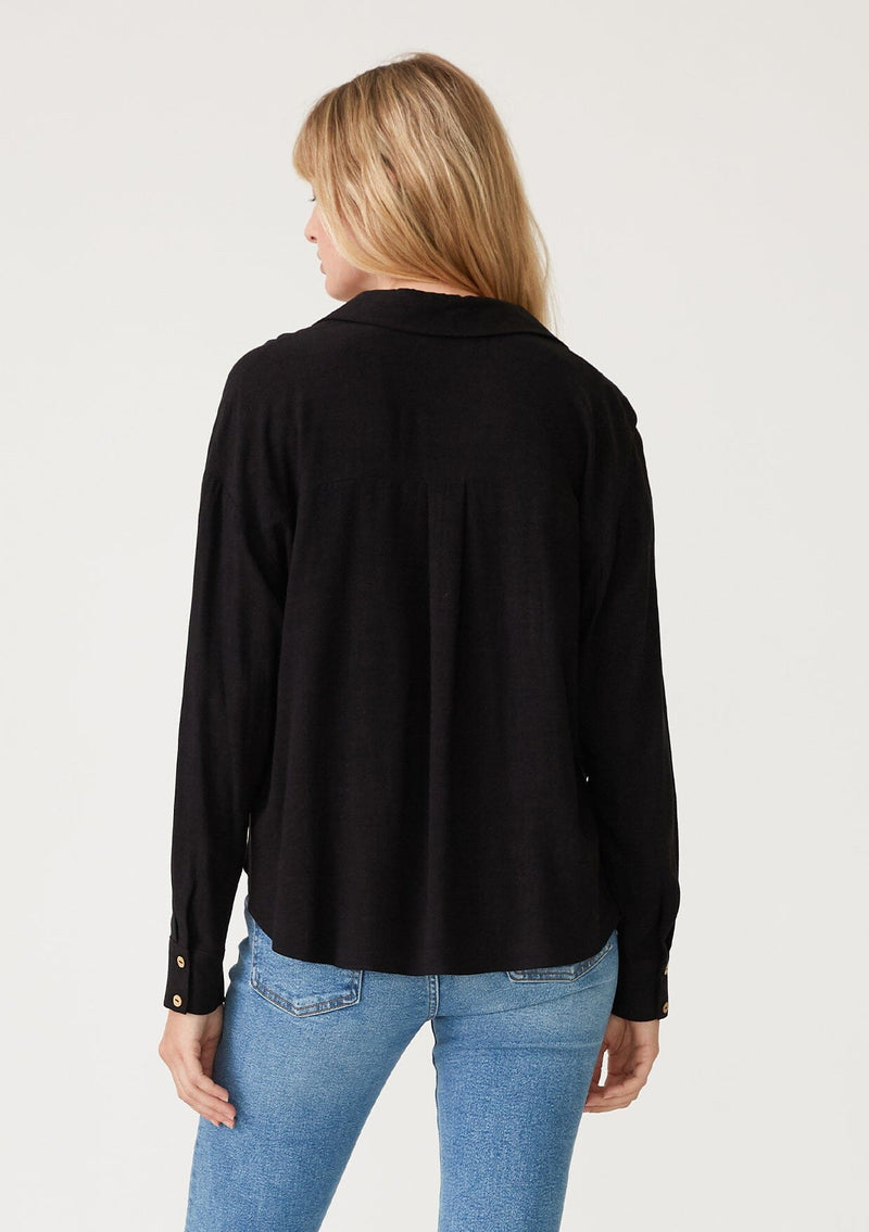 [Color: Black] A back facing image of a blonde model wearing a black linen blend relaxed button up shirt. With long sleeves, a dropped shoulder, a collared v neckline, a high low hemline, and a knot front waist detail.
