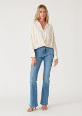 [Color: Vanilla] A full body front facing image of a blonde model wearing an ivory linen blend relaxed button up shirt. With long sleeves, a dropped shoulder, a collared v neckline, a high low hemline, and a knot front waist detail. 