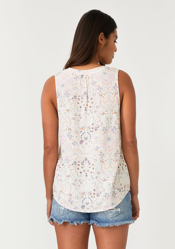 [Color: Natural/Pink] A back facing image of a brunette model wearing a relaxed bohemian resort tank top in a natural and pink floral print. With a v neckline, sheer lattice trim, and a soft hand feel. 