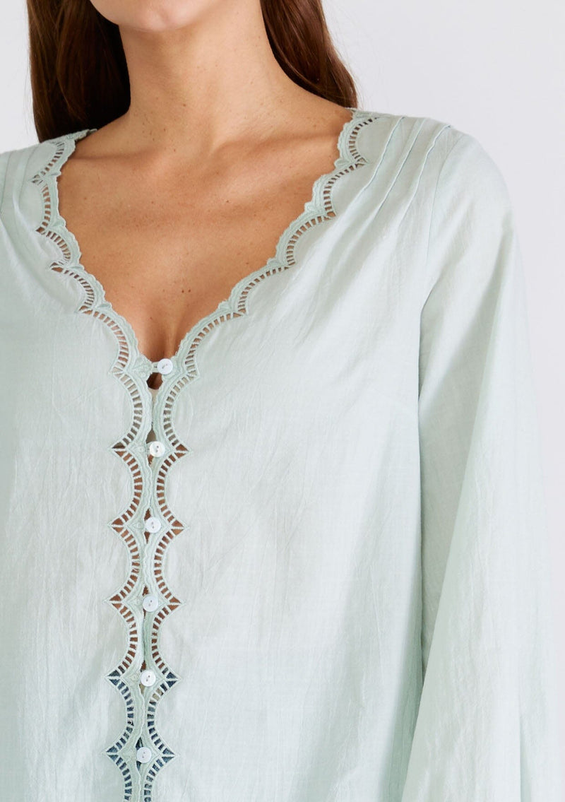 [Color: Dusty Seafoam] A close up front front facing image of a brunette model wearing a feminine spring blouse in dusty seafoam. With scalloped embroidered lace trim, a button front, a v neckline, and long sleeves with elastic wrist cuffs. 