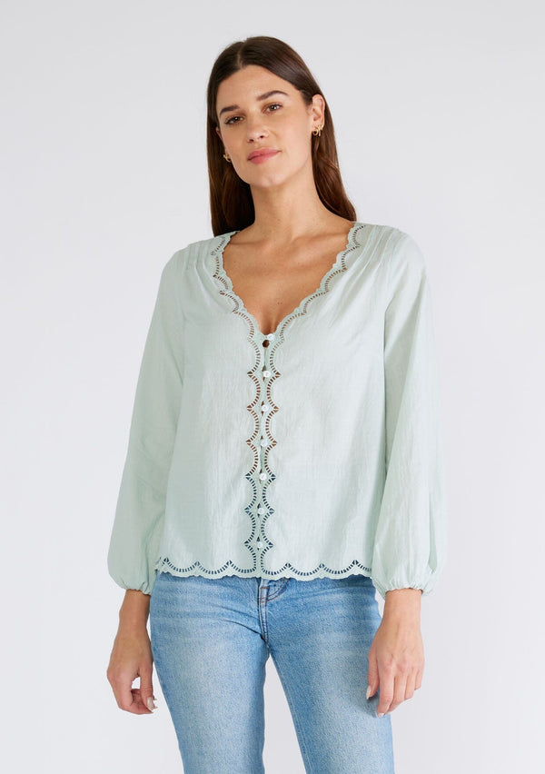 [Color: Dusty Seafoam] A front facing image of a brunette model wearing a feminine spring blouse in dusty seafoam. With scalloped embroidered lace trim, a button front, a v neckline, and long sleeves with elastic wrist cuffs. 