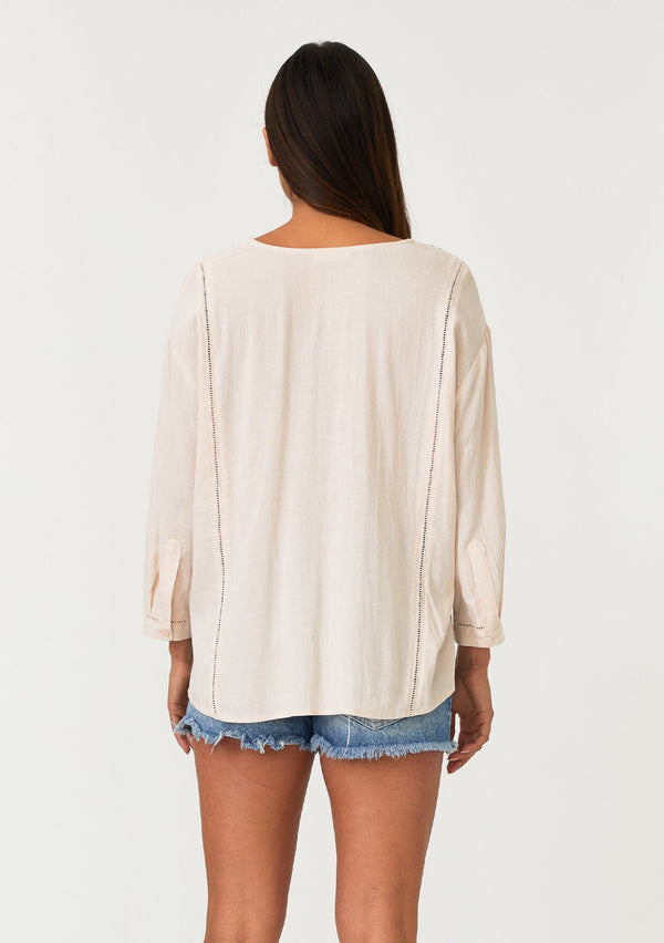 [Color: Light Peach] A back facing image of a brunette model wearing a bohemian light pink button front blouse crafted from a linen blend. With long three quarter length sleeves, a round neckline, and delicate pleated details throughout.