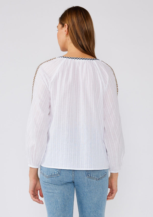 [Color: White/Gold] A back facing image of a brunette model wearing a white cotton bohemian blouse with gold sequined details. With long sleeves, a split v neckline, contrast embroidery, and a relaxed fit. 