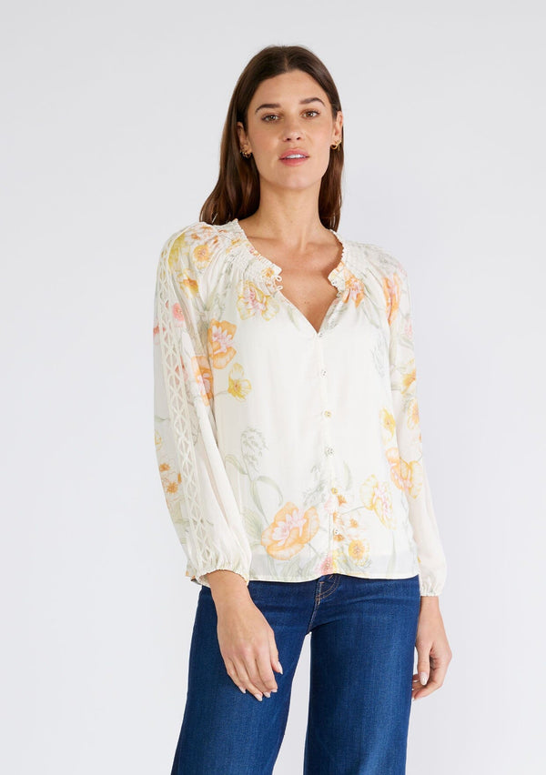[Color: Vanilla/Coral] A front facing image of a brunette model wearing a beautiful bohemian chic spring blouse in an ivory and coral floral print. With long raglan sleeves, a smocked round neckline, a self covered button front, and a front keyhole. 