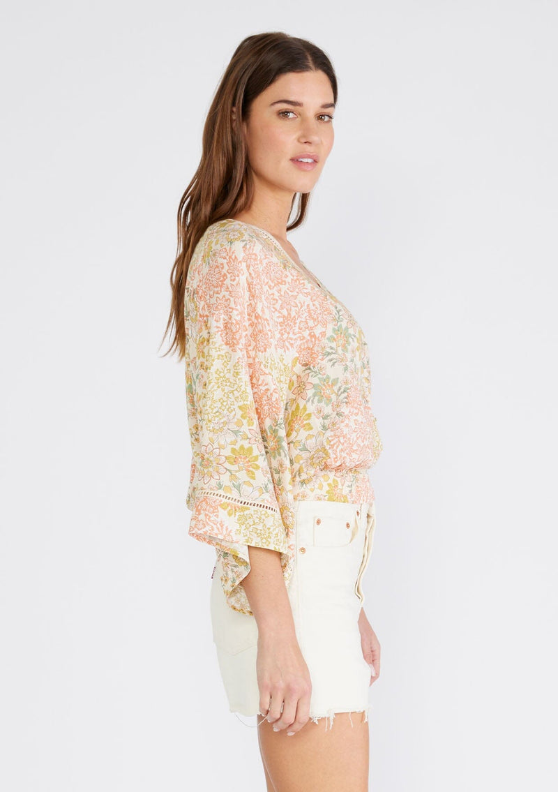 [Color: Dusty Peach/Rust] A side facing image of a brunette model wearing a classic button front bohemian top with dramatic billowy half length sleeves, designed in a peach and rust mixed floral print. With a v neckline, sheer lattice trim, and a slightly cropped length.