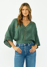 [Color: Forest Green] A front facing image of a brunette model wearing a green bohemian top with tonal embroidery, wide sleeves, lattice trims, a button front, and a v neckline. 