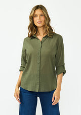 [Color: Olive] A front facing image of a blonde model wearing a green button front shirt crafted in a sheer textured cotton. Featuring a collared neckline, high low hemline, and long roll tab sleeves. Paired with a dark wash denim. 