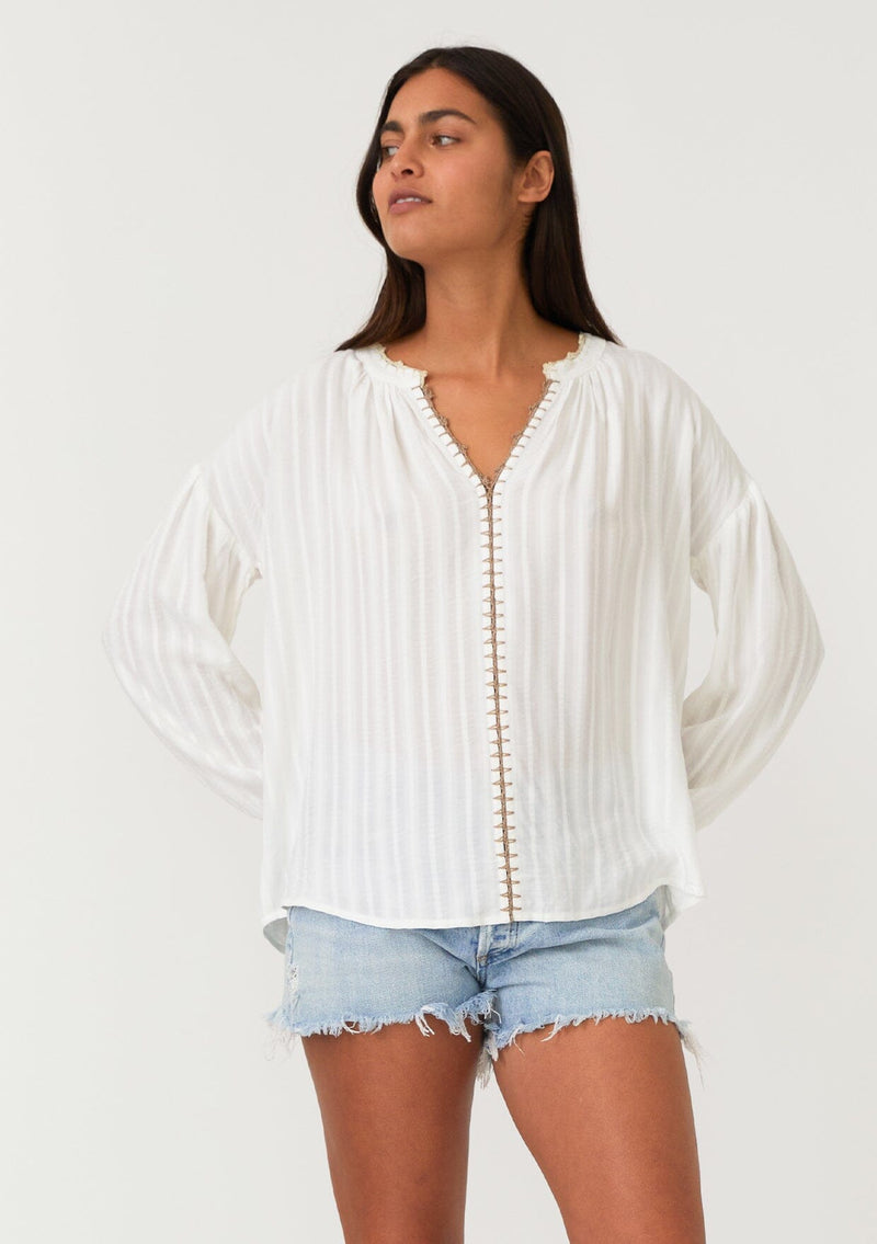 [Color: White/Taupe] A front facing image of a brunette model wearing a bohemian white blouse. With long sleeves, a dropped shoulder, a v neckline, and contrast crochet trim. 