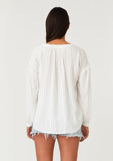 [Color: White/Taupe] A back facing image of a brunette model wearing a bohemian white blouse. With long sleeves, a dropped shoulder, a v neckline, and contrast crochet trim. 