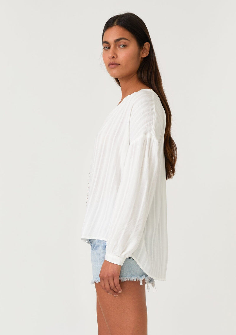 [Color: White/Taupe] A side facing image of a brunette model wearing a bohemian white blouse. With long sleeves, a dropped shoulder, a v neckline, and contrast crochet trim. 