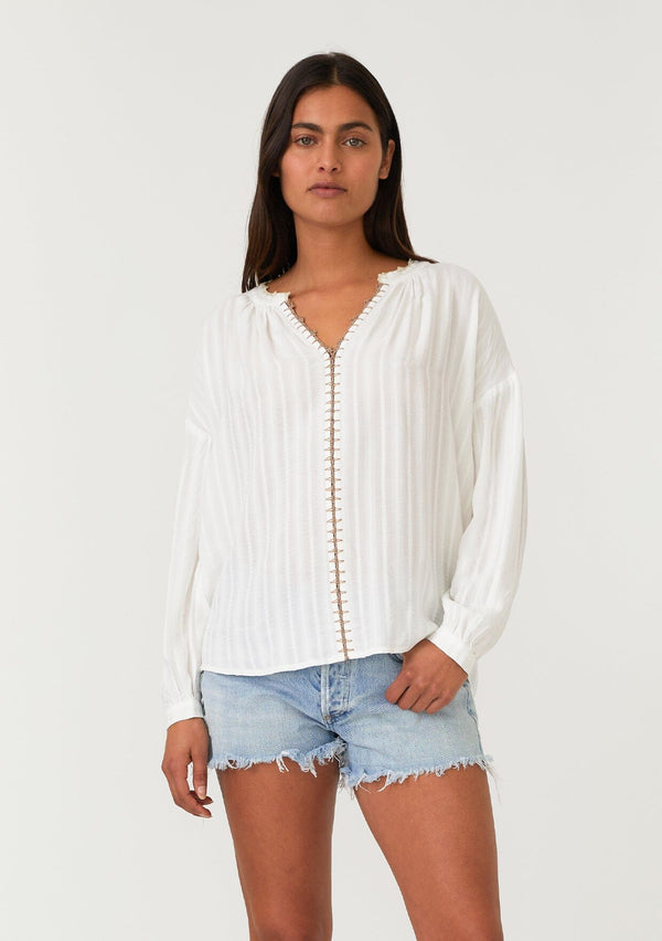 [Color: White/Taupe] A front facing image of a brunette model wearing a bohemian white blouse. With long sleeves, a dropped shoulder, a v neckline, and contrast crochet trim. 
