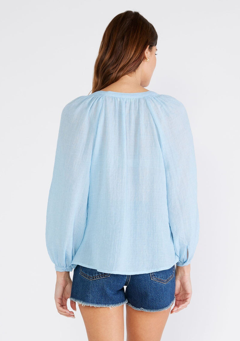 [Color: Light Blue] A back facing image of a brunette model wearing a light blue sheer bohemian blouse with long raglan sleeves, a round neckline, a button front, and a relaxed fit. 