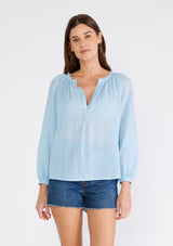 [Color: Light Blue] A front facing image of a brunette model wearing a light blue sheer bohemian blouse with long raglan sleeves, a round neckline, a button front, and a relaxed fit. 
