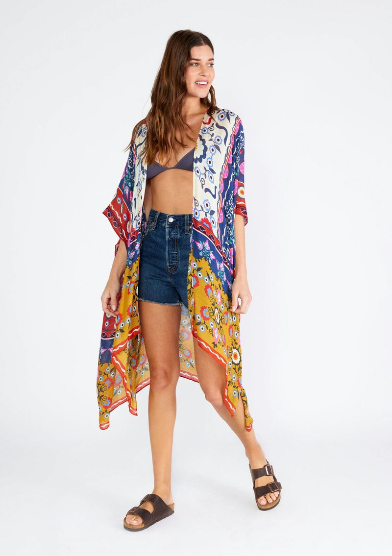 [Color: Natural/Mustard] A full body front facing image of a brunette model wearing a lightweight bohemian mid length kimono in a mixed floral print. A brightly multi colored style with half length sleeves, an open front, and side slits. Perfect for the beach as a swim cover up or around the house as a lounge robe. 