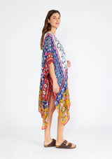 [Color: Natural/Mustard] A side facing image of a brunette model wearing a lightweight bohemian mid length kimono in a mixed floral print. A brightly multi colored style with half length sleeves, an open front, and side slits. Perfect for the beach as a swim cover up or around the house as a lounge robe. 