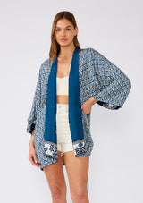 [Color: Indigo/Blue] A half body front facing image of a brunette model wearing a bohemian kimono in an indigo blue print. With three quarter length long sleeves, an open front, and a mid length. A reversible cover up for the beach or pool side. 