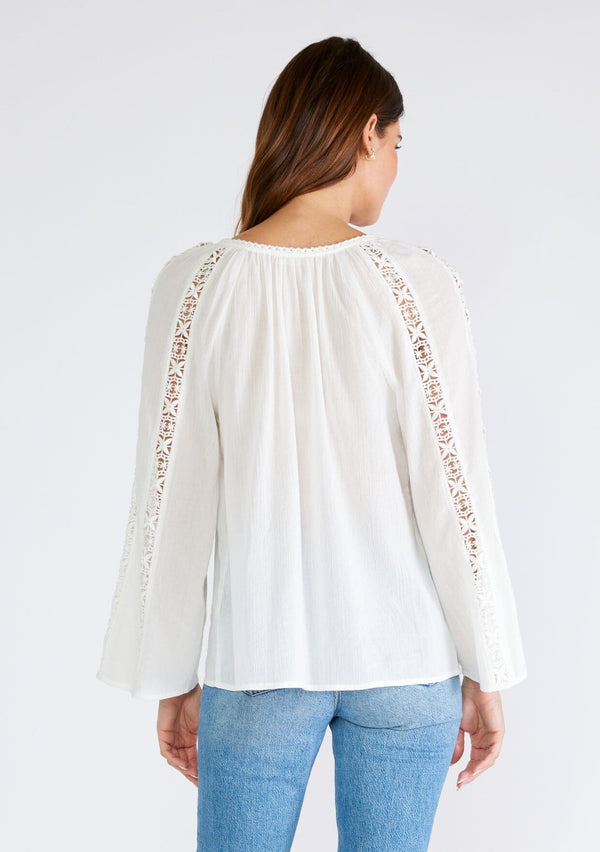 [Color: White] A back facing image of a brunette model wearing a classic bohemian white cotton blouse. With crochet trim, a split v neckline, and long bell sleeves. 