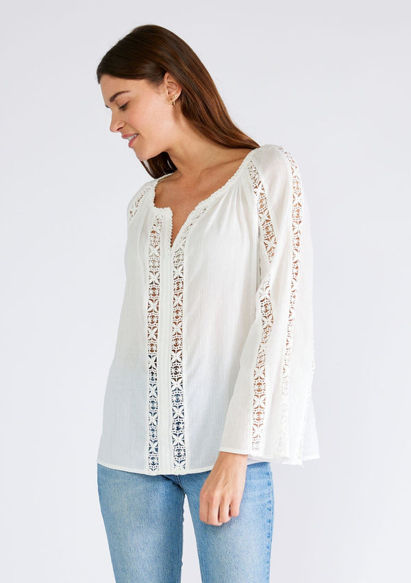 [Color: White] A front facing image of a brunette model wearing a classic bohemian white cotton blouse. With crochet trim, a split v neckline, and long bell sleeves. 