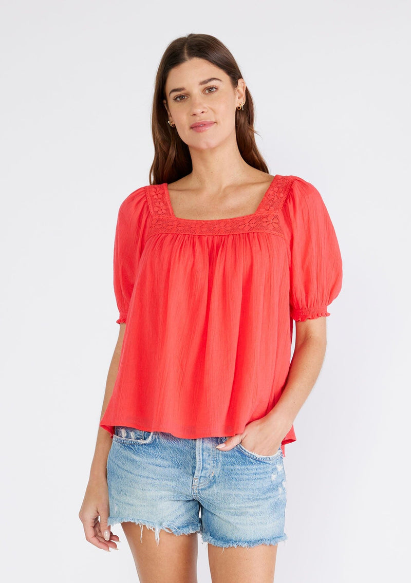 [Color: Hibiscus] A half body front facing image of a brunette model wearing a bright red cotton bohemian top with short puff sleeved, a ruffled elastic cuff, a square neckline, and lace trim. 