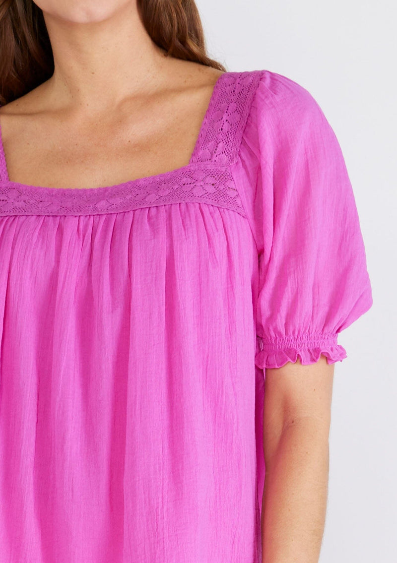 [Color: Orchid] A close up front facing image of a brunette model wearing a bright purple cotton bohemian top with short puff sleeved, a ruffled elastic cuff, a square neckline, and lace trim. 