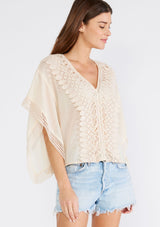 [Color: Light Peach] A front facing image of a brunette model wearing a sheer light peach bohemian beach cover up top. With crochet lace trim, short sleeves, a v neckline, and a relaxed, boxy fit. Perfect for the beach or wearing over your swimsuit on your next vacation.