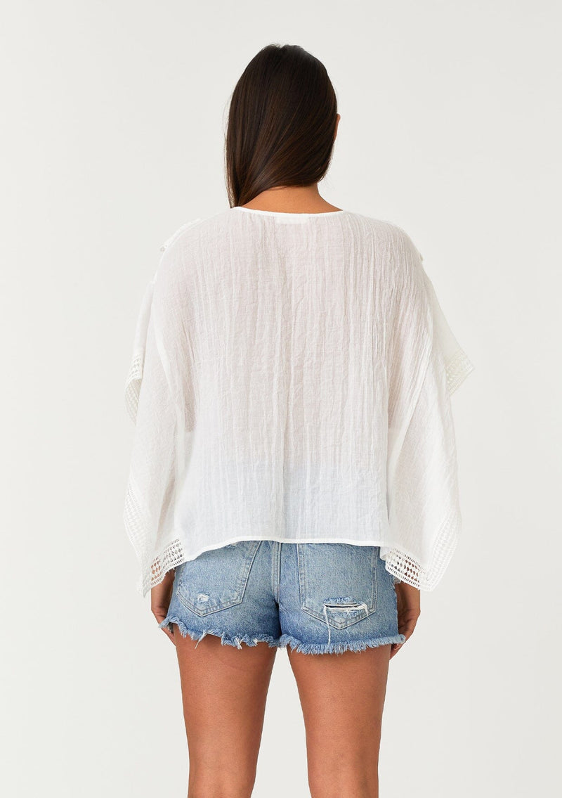 [Color: Off White] A back facing image of a brunette model wearing a sheer white bohemian beach cover up top. With crochet lace trim, short sleeves, a v neckline, and a relaxed, boxy fit. Perfect for the beach or wearing over your swimsuit on your next vacation. 