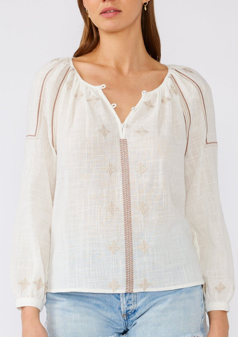 [Color: White/Taupe] A close up front facing image of a brunette model wearing a white cotton bohemian blouse with taupe brown embroidered details. With long sleeves, a round neckline, a button front, and a relaxed fit. 