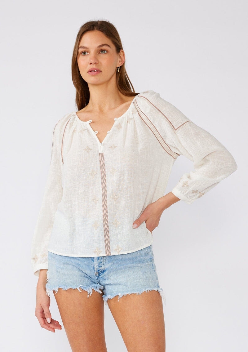 [Color: White/Taupe] A front facing image of a brunette model wearing a white cotton bohemian blouse with taupe brown embroidered details. With long sleeves, a round neckline, a button front, and a relaxed fit. 
