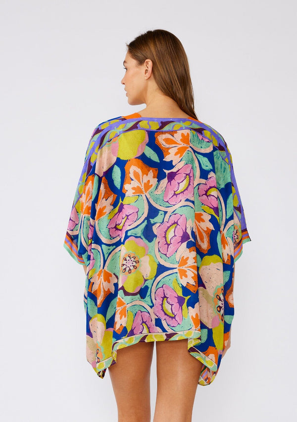 [Color: Blue/Coral] A back facing image of a brunette model wearing a bohemian style kimono top in a bright blue and coral floral print with a contrast orange border. A lightweight beach cover up with half length kimono sleeves, an open front, and a hip length hemline. 