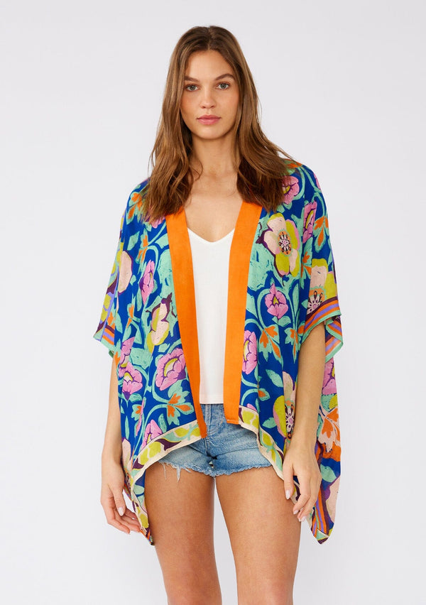 [Color: Blue/Coral] A front facing image of a brunette model wearing a bohemian style kimono top in a bright blue and coral floral print with a contrast orange border. A lightweight beach cover up with half length kimono sleeves, an open front, and a hip length hemline. 