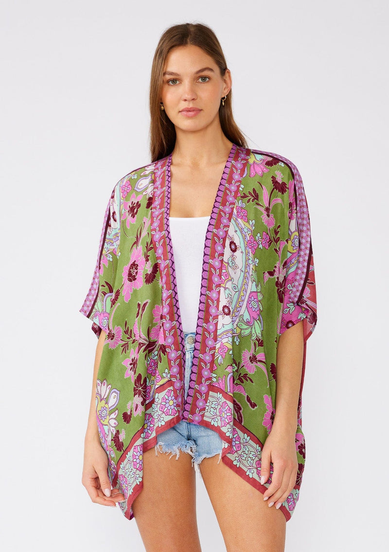 [Color: Green/Rose] A front facing image of a brunette model wearing a bohemian style kimono top in a green and pink floral print, with contrast border. A lightweight beach cover up with half length kimono sleeves, an open front, and a hip length hemline. 