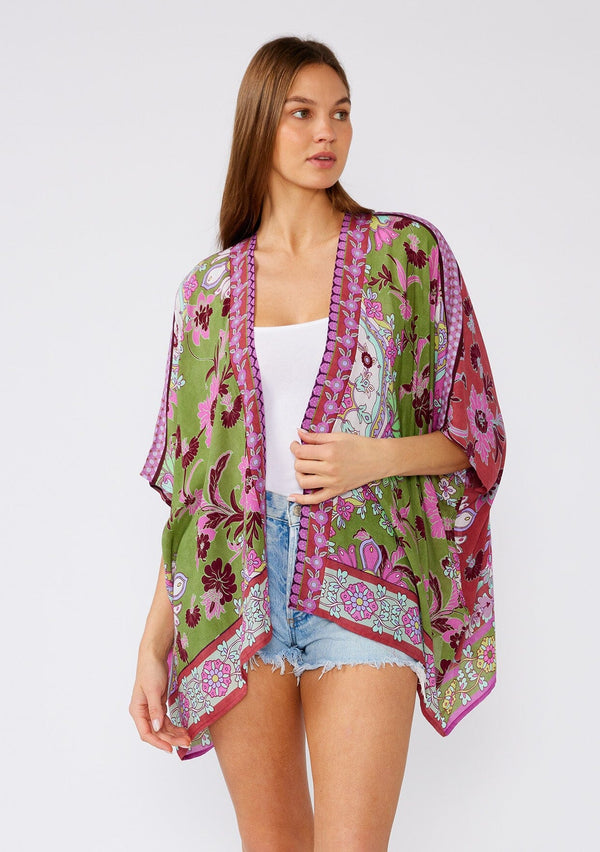 [Color: Green/Rose] A half body front facing image of a brunette model wearing a bohemian style kimono top in a green and pink floral print, with contrast border. A lightweight beach cover up with half length kimono sleeves, an open front, and a hip length hemline. 