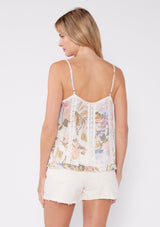 [Color: Off White/Periwinkle] A back facing image of a blonde model wearing a pretty bohemian camisole in an off white and periwinkle blue floral print. With lace trim, adjustable spaghetti straps, a v neckline, and a ruffled hemline. 