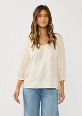 [Color: Cream] A front facing image of a brunette model wearing a cream bohemian embroidered blouse with a v-neckline and 3/4 length sleeves with ruffled cuffs. 