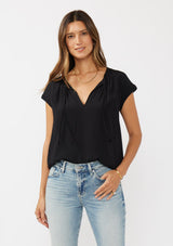 [Color: Black] A brunette model wearing a relaxed fit  black top. With self neck ties, ruched split v neckline, and short dolman sleeves. Styled with a cute vintage denim for a laid back look. 