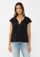 [Color: Black] A front facing image of a brunette model wearing a relaxed fit  black top. With self neck ties, ruched split v neckline, and short dolman sleeves. Styled with a cute vintage denim for a laid back look. 