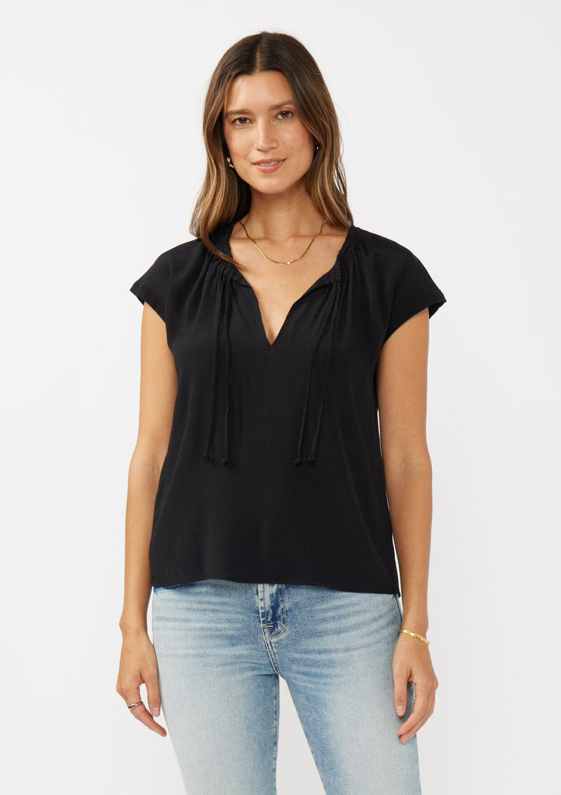 [Color: Black] A front facing image of a brunette model wearing a relaxed fit  black top. With self neck ties, ruched split v neckline, and short dolman sleeves. Styled with a cute vintage denim for a laid back look. 