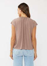 [Color: Mocha] A back facing image of a brunette model wearing a relaxed fit  brown mocha top. With self neck ties, ruched split v neckline, and short dolman sleeves. Styled with a cute wide leg denim for a laid back look. 