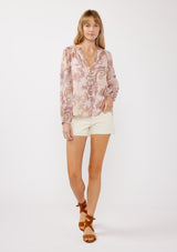 [Color: Blush/Rose] A front facing image of a blonde model wearing a paisley floral print blouse with gold foil accents. Featuring a split v-neckline, long sleeves, a button front, pintuck details, and ruffle trim details. 