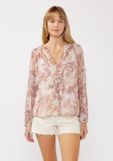 [Color: Blush/Rose] A front facing image of a blonde model wearing a paisley floral print blouse with gold foil accents. Featuring a split v-neckline, long sleeves, a button front, pintuck details, and ruffle trim details. 