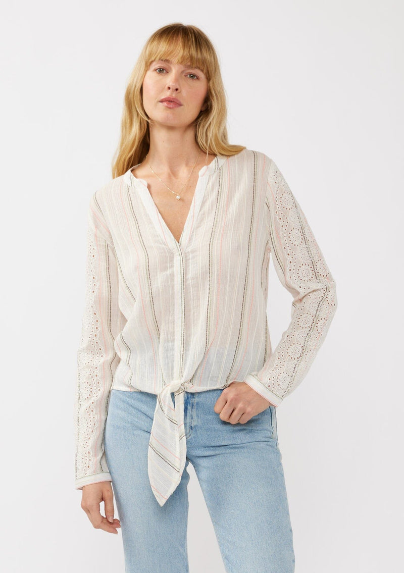 [Color: White/Coral] A front facing image of a blonde model wearing an off white yarn dye stripe top with embroidered eyelet details. This sheer  cotton top features a split v-neckline, long sleeves, button cuff closures, and a tie front hem detail. Perfect for vacation and resort styling. 