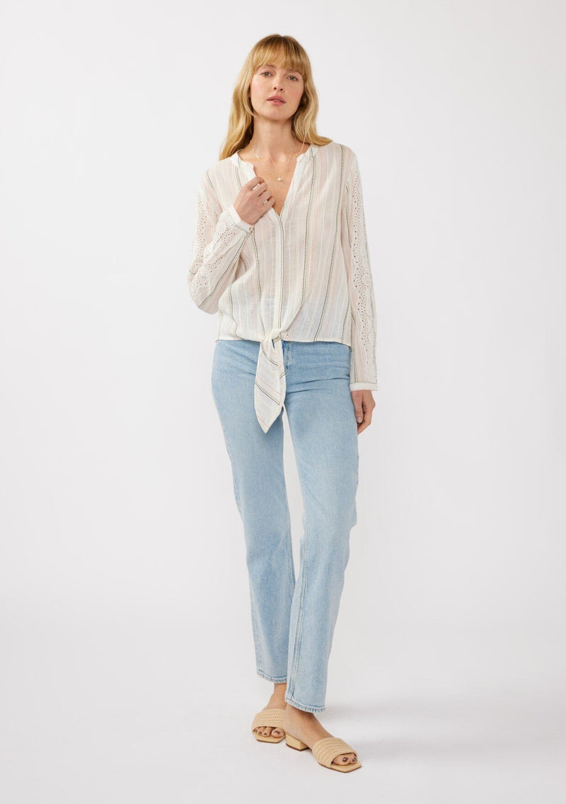 [Color: White/Coral] A front facing image of a blonde model wearing an off white yarn dye stripe top with embroidered eyelet details. This sheer  cotton top features a split v-neckline, long sleeves, button cuff closures, and a tie front hem detail. Perfect for vacation and resort styling. 