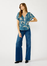 [Color: Teal/Blue] A front facing image of a blonde model wearing a lightweight  teal floral shirt with a split v-neckline and short sleeves. An effortless fall top for casual outings. 