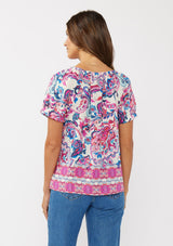 [Color: Natural/Dusty Pink] A back facing image of a brunette model wearing a vibrant floral print boho top with an elastic neckline and short puff sleeves.