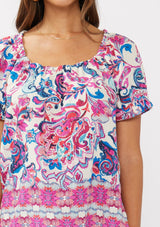 [Color: Natural/Dusty Pink] A detail image of a brunette model wearing a vibrant floral print boho top with an elastic neckline and short puff sleeves.