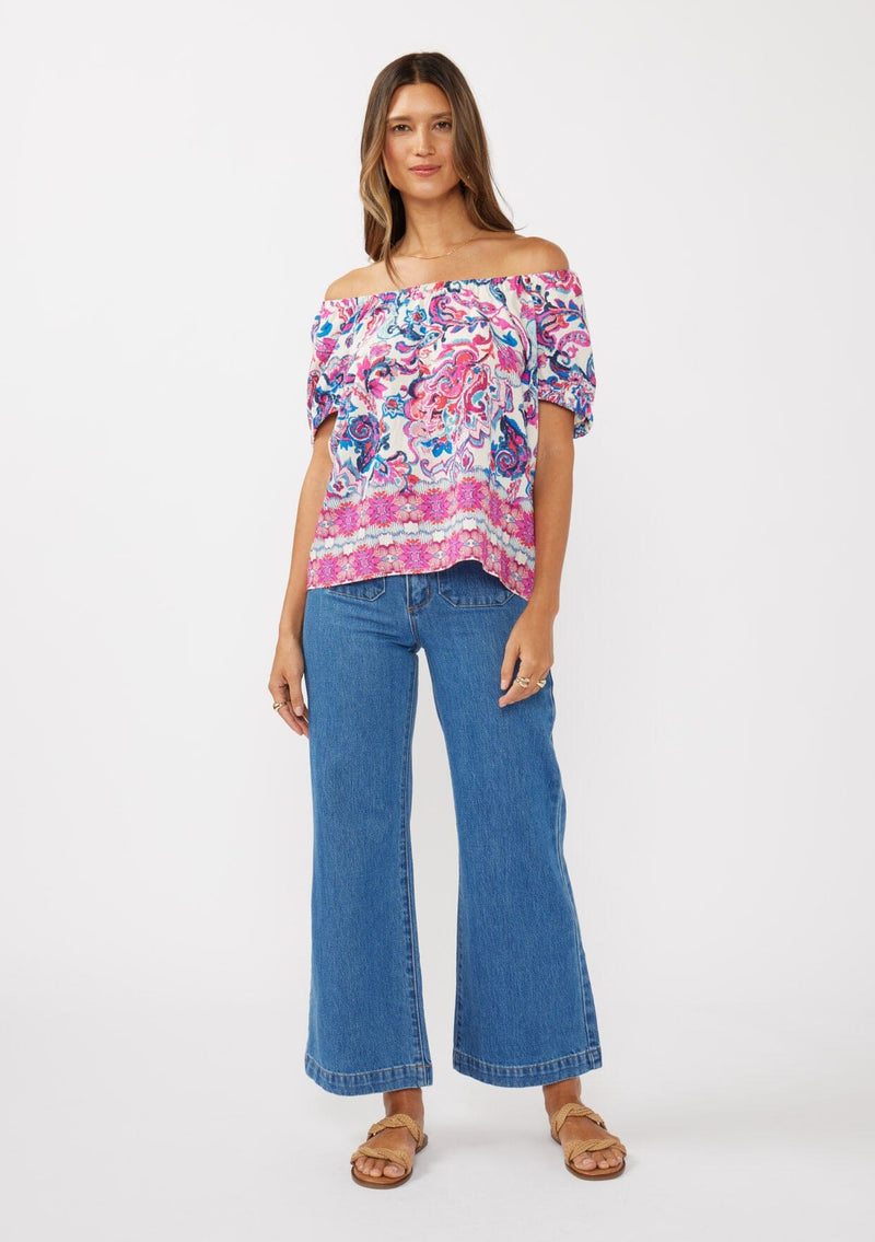 [Color: Natural/Dusty Pink] A front facing image of a brunette model wearing an off shoulder vibrant floral print boho top with an elastic neckline and short puff sleeves.