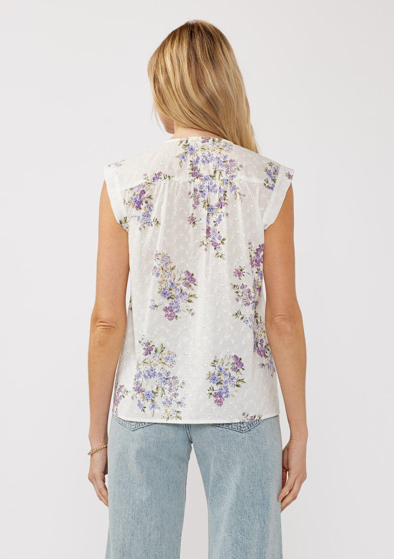 [Color: Off White/Lilac] A back-facing image of a blonde model wearing a white top adorned with a purple floral print and embroidered eyelet accents. This spring top features a button-front neck closure and delicate pintuck details.